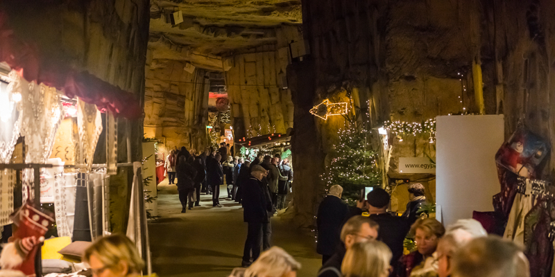 Doorkijkje van mergelgangen met daarin shoppende mensen aan verschillende kerststands in kerstmarkt Gemeentegrot