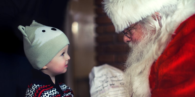 Jongetje met Noorse trui en dierenmuts kijkt kerstman in de ogen