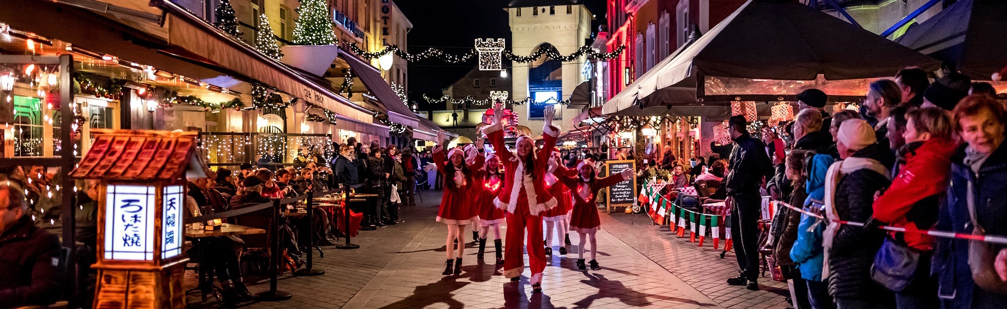 Groep kerstmeisjes dansend door de straten van Valkenburg terwijl publiek naar hen kijkt.